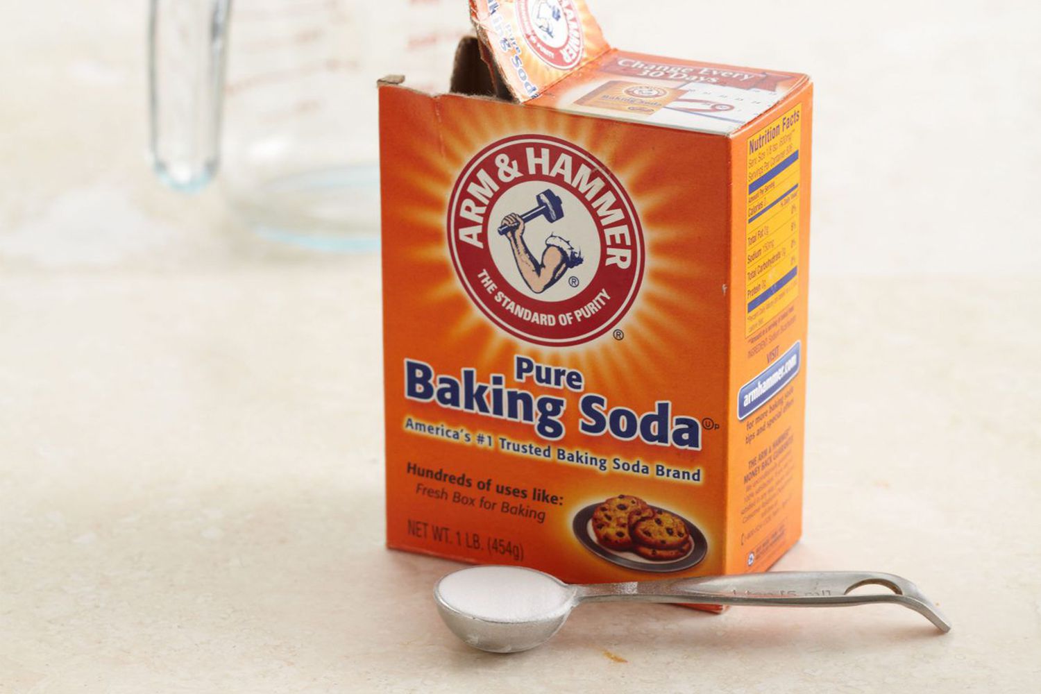 A box of Arm & Hammer pure baking soda with a measuring spoon of the powder in front of it.